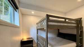 A bunk bed with a wooden frame, a bedside table with a lamp, and a window with blinds. - Zénitude En Forêt Chalet – Spa & Precious Moments (Saint-Damien-de-Buckland)