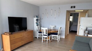 Una sala de estar con televisor, cómoda de madera, mesa de comedor con sillas y un sofá gris.