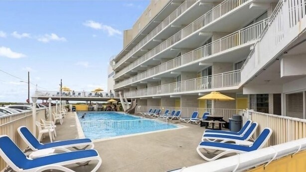 Un área de piscina con tumbonas y una piscina pequeña, rodeada por un edificio con balcones.