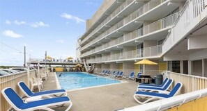 A pool area with sun loungers and a small pool, surrounded by a building with balconies.