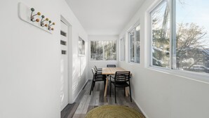 A bright, white-walled room with a wooden dining table and chairs, large windows with a view of trees and a snowy landscape. - The Grove 1/2 mile from Boyne Mountain Sleeps 4 (Boyne Falls)