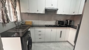 Een kleine keuken met witte kastjes, een roestvrijstalen spoelbak, een magnetron en een fornuis.