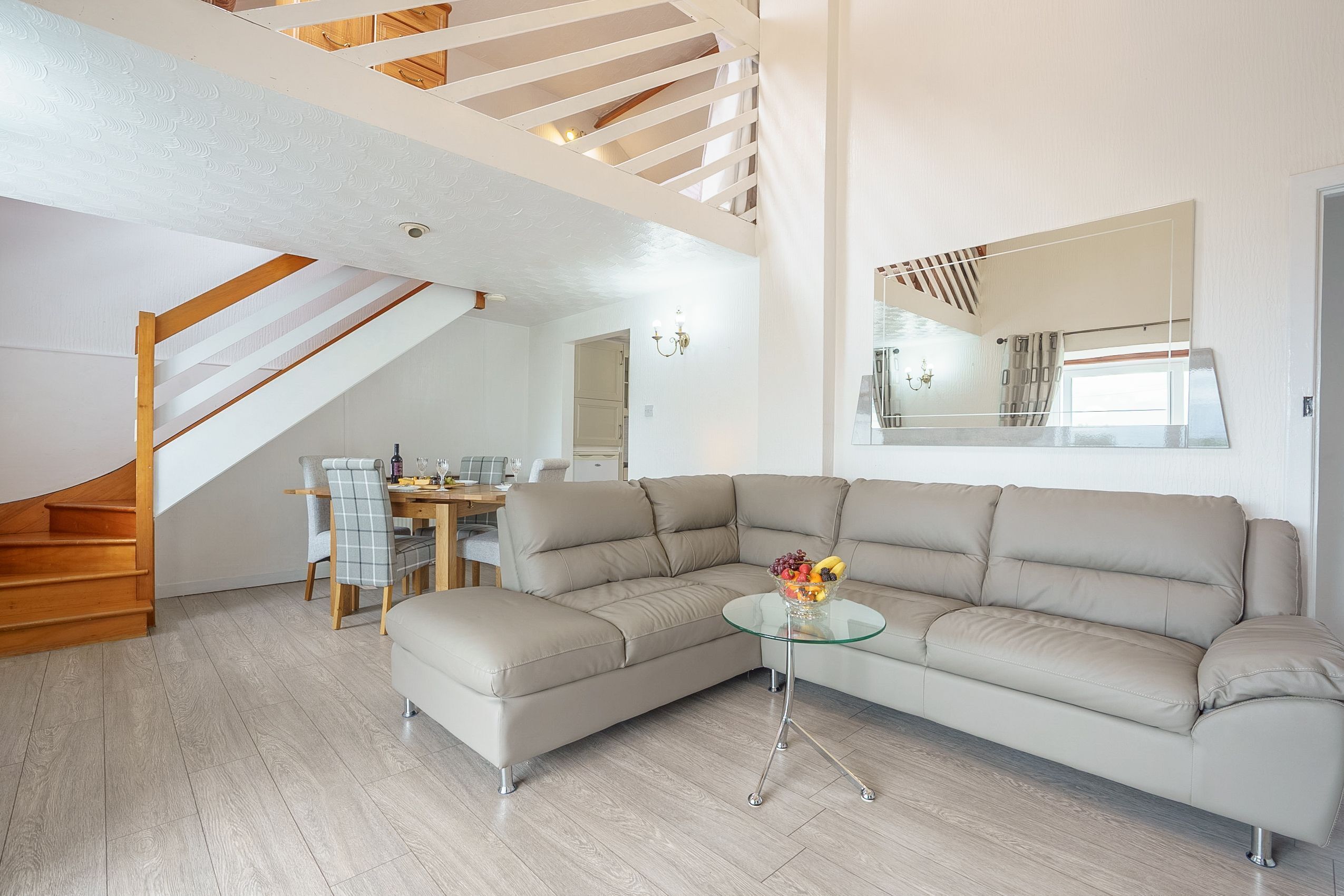 A modern living room with a sectional sofa, a glass coffee table, and a dining area with a wooden table and chairs.