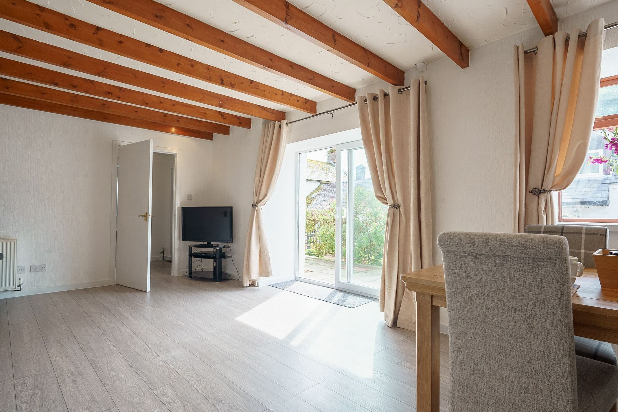 Una habitación amplia con techo de madera, televisor y puerta corrediza de vidrio que da a un espacio exterior.