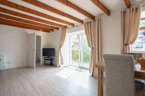 A spacious room with a wooden ceiling, a television, and a sliding glass door leading to an outdoor area. - Morton Cottage - a cottage that sleeps 2 guests  in 1 bedroom (Thornhill)
