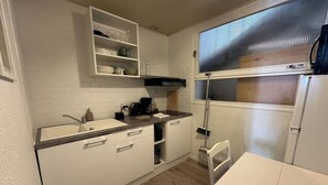 A compact kitchen with white cabinets, a countertop, a sink, a window with blinds, and a small dining table. - Serenity - In the heart of the Dax thermal baths (Dax)