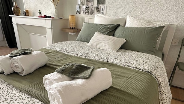 A neatly made bed with green and white bedding, a bedside table with a lamp, and a wall with framed artwork. - Serenity - In the heart of the Dax thermal baths (Dax)