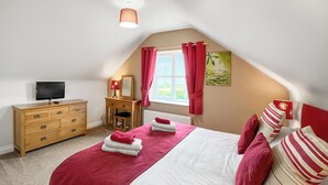 Une chambre à coucher comprenant un lit, une commode en bois, un bureau, une chaise, un téléviseur et une fenêtre avec des rideaux.