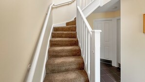 Un escalier recouvert de moquette, avec des rampes blanches et une porte blanche en bas.