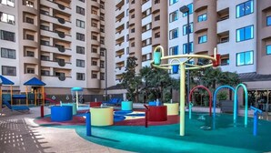 Un espace de jeux intérieur doté de structures colorées et d’une zone avec piscine, le tout entouré d’immeubles d’habitation de grande hauteur.