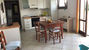 A compact kitchen with white cabinets, a dining table with chairs, and a small window with curtains.