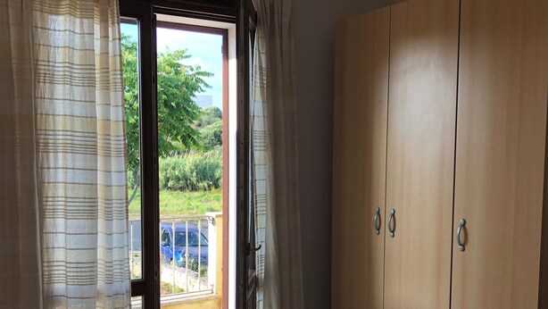 A room with a sliding glass door leading to a balcony, a wooden wardrobe, and a bed.