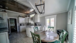Una cocina amplia con armarios blancos, una isla de madera y un comedor con sillas verdes.