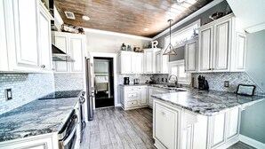 Una cocina amplia con armarios blancos, encimera de mármol y techo de madera.