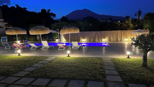 A poolside area with lounge chairs, umbrellas, and a pool with blue lighting. - Relaxation with Jacuzzi and pool between Pompeii Amalfi coast, Sorrento and Capri (Trecase)