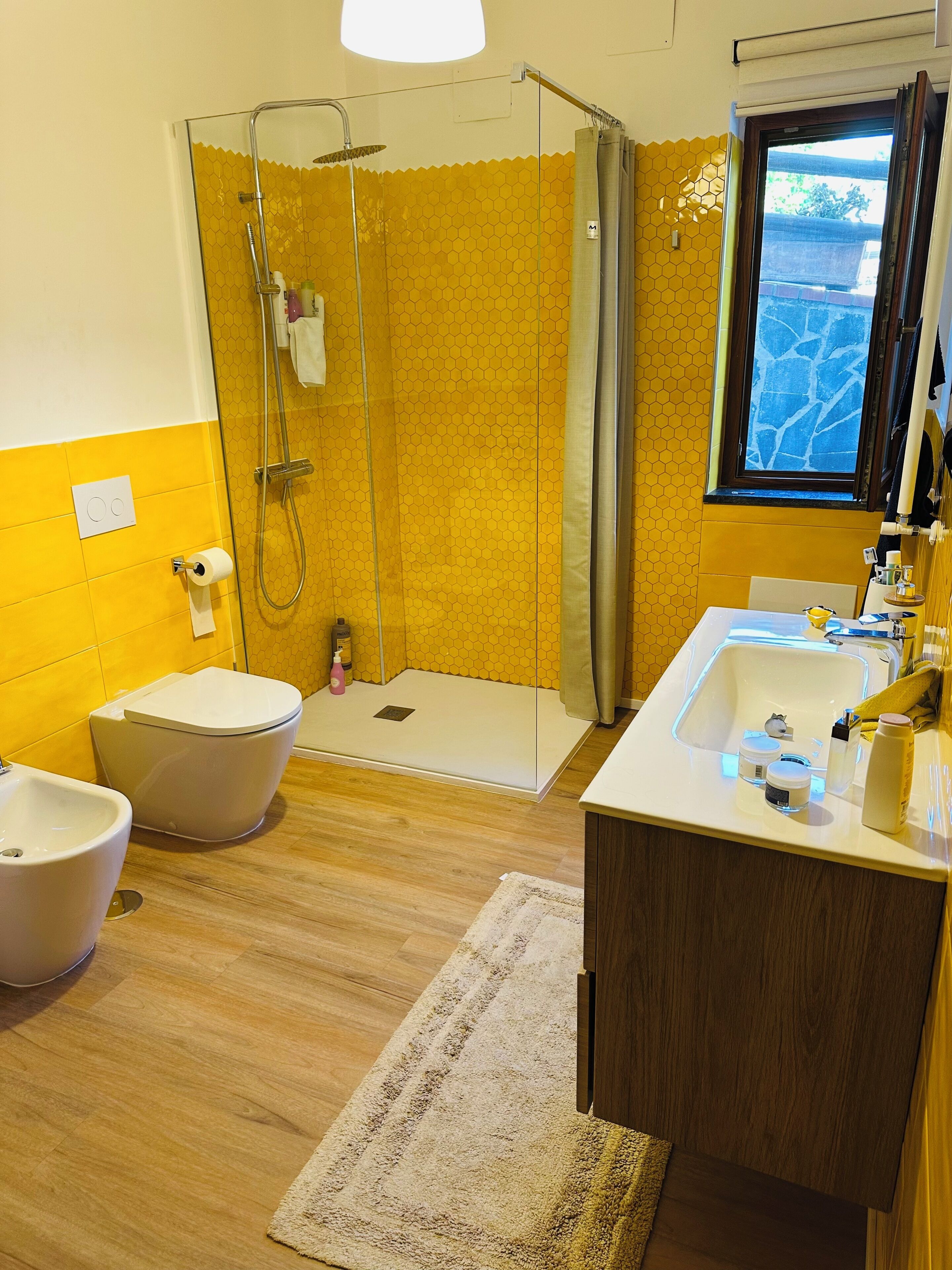 A bathroom with a glass-enclosed shower, a toilet, a bidet, and a sink with toiletries.
