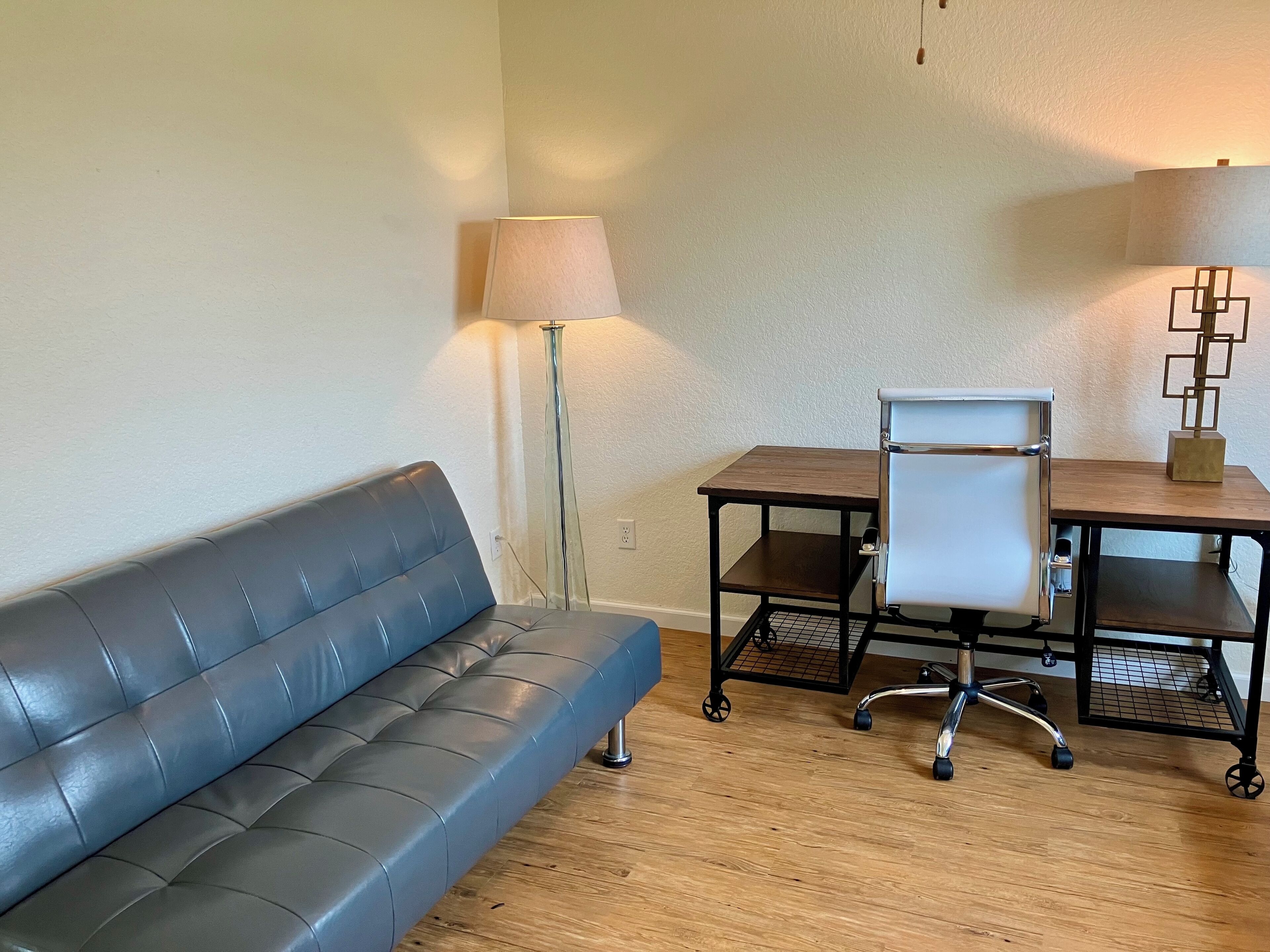 A room with a leather sofa, a wooden table with a chair, and two floor lamps.
