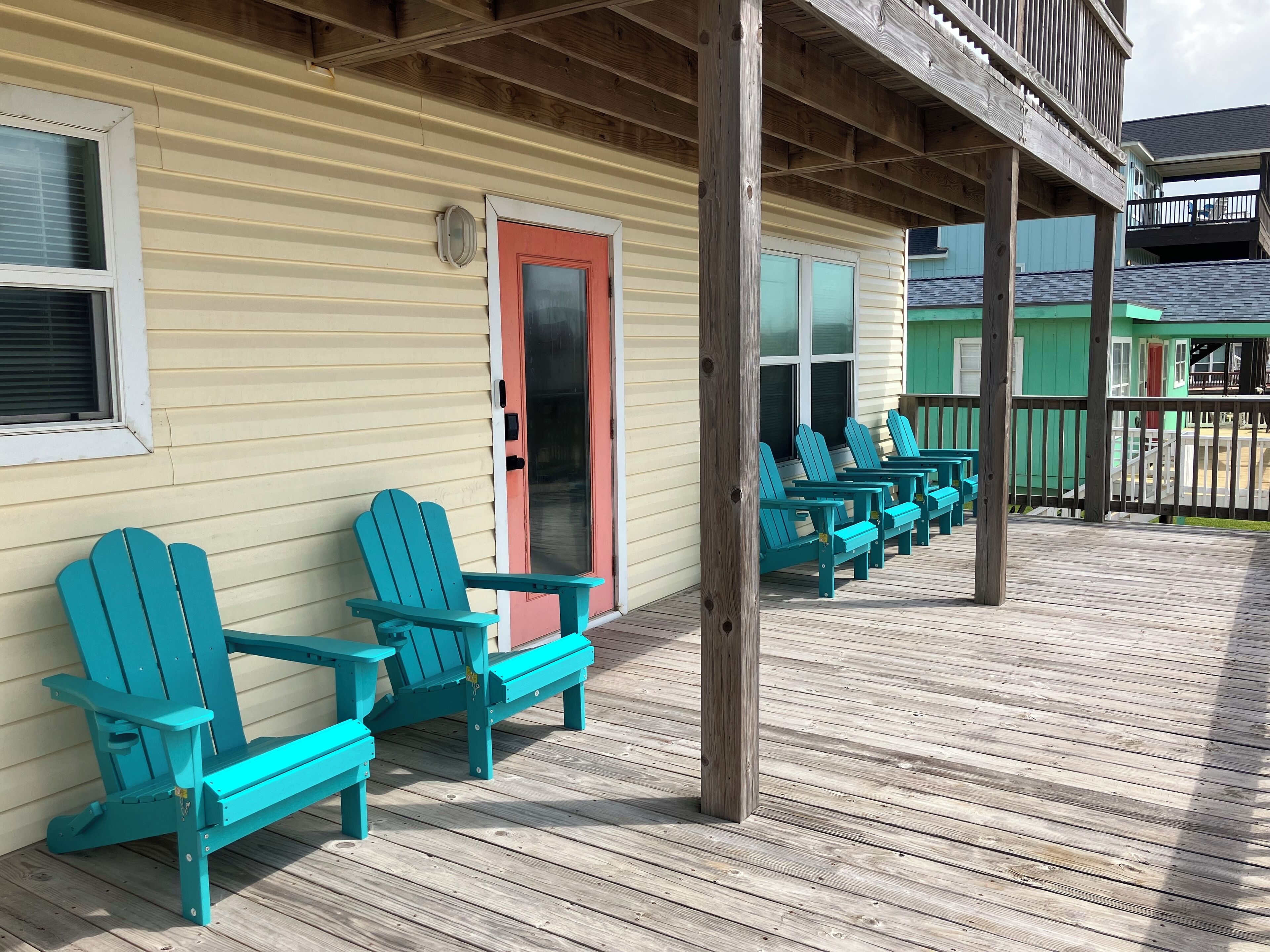 A wooden deck with turquoise Adirondack chairs and a wooden railing.