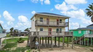 A two-story house with a balcony, a satellite dish, and a wooden deck. - The Neon Palm - 4bed 3bath in Surfside Beach TX (Freeport)