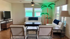 A modern living room with a dining table, two chairs, a sofa, a TV, and a ceiling fan. - The Neon Palm - 4bed 3bath in Surfside Beach TX (Freeport)