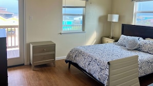 A bedroom with a bed, a nightstand, a lamp, a ceiling fan, and a window with a view of a balcony. - The Neon Palm - 4bed 3bath in Surfside Beach TX (Freeport)