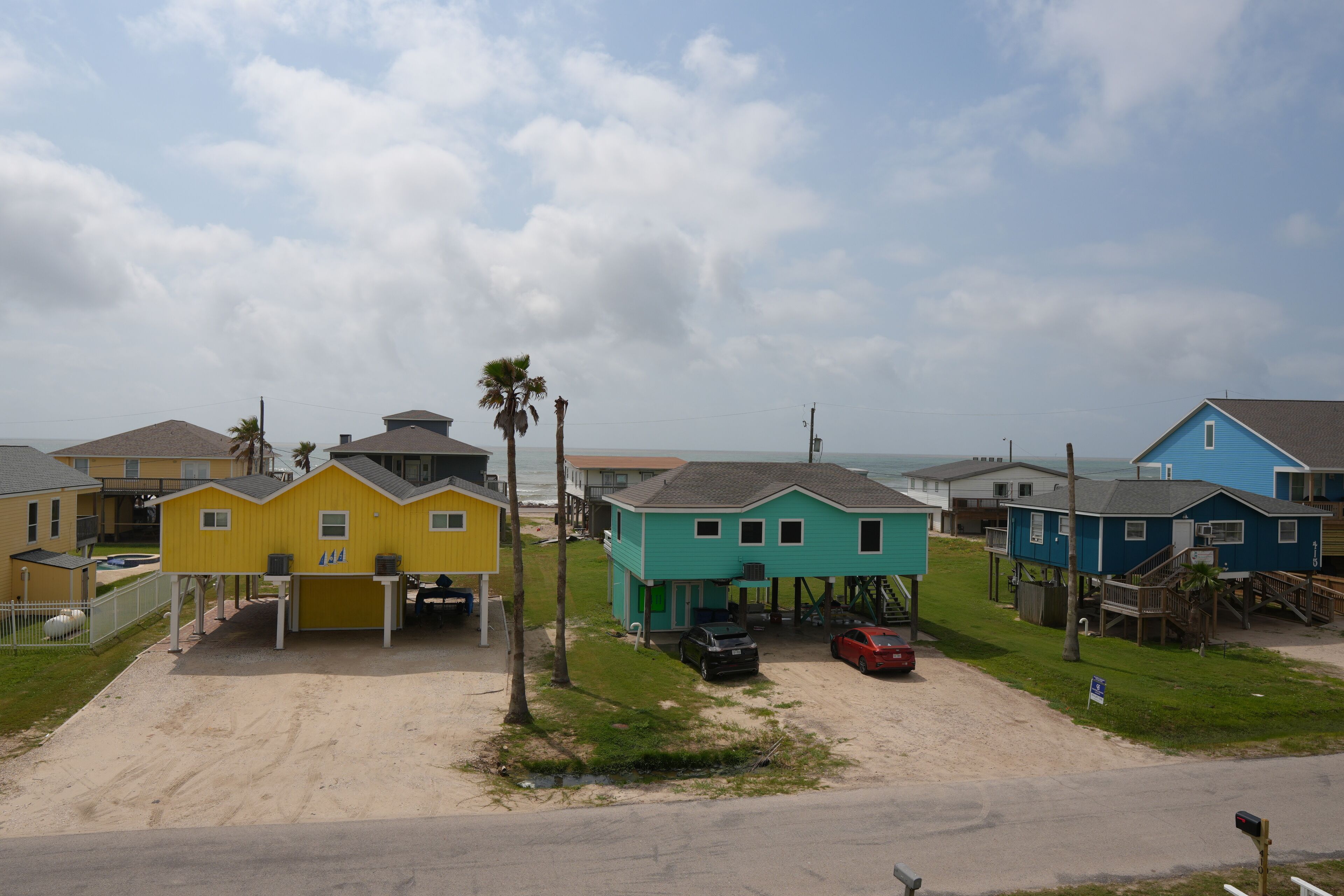 A coastal residential area with colorful houses, a sandy driveway, and a clear sky.