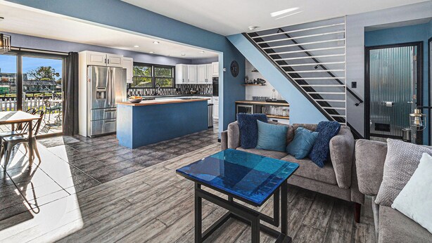 Una cocina moderna con una isla central, un área de comedor con una mesa y sillas, y una escalera que sube a un nivel superior.
