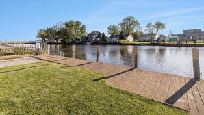 Zona residencial a orillas del río, con casas, un muelle de madera y un césped.
