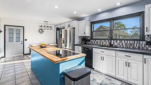 Una cocina moderna con una isla azul, electrodomésticos de acero inoxidable, armarios blancos y un amplio ventanal.