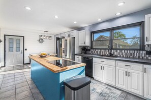 Una cucina moderna con isola blu, elettrodomestici in acciaio inossidabile, mobili bianchi e un'ampia finestra.
