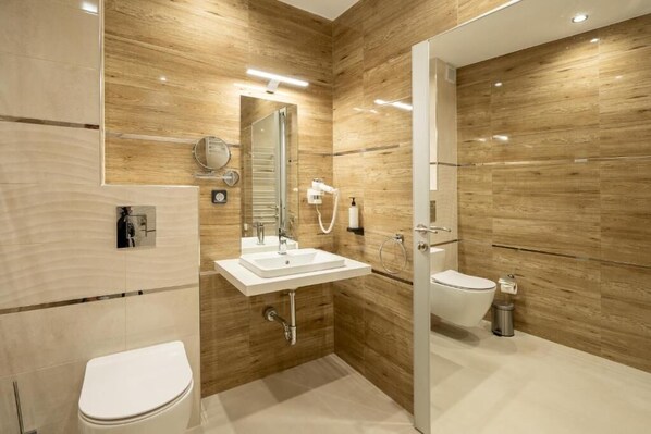A modern bathroom with a wooden wall, a white sink, a toilet, and a glass shower enclosure. - K&G City Hotel  (Kazanlak)