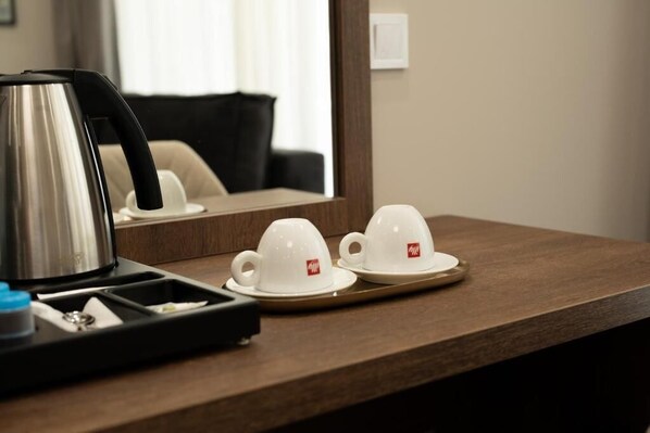A hotel room with a wooden table, a kettle, and two white cups with a logo on them. - K&G City Hotel  (Kazanlak)