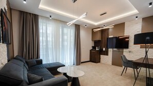 Un soggiorno moderno con un divano, due tavolini, una TV e un angolo cucina dotato di TV a schermo piatto e una lampada.