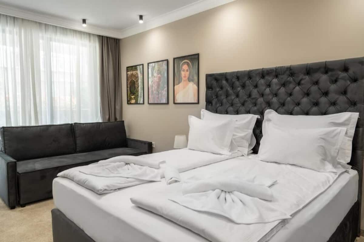 Ein Hotelzimmer mit einem großen Bett, einer schwarzen Ledersofa und drei gerahmten Bildern an der Wand.