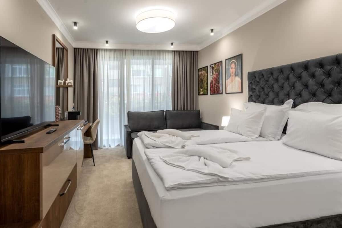 Ein Hotelzimmer mit einem großen Bett, einem Schreibtisch mit Stuhl, einem Fernseher und einem Fenster mit Vorhängen.