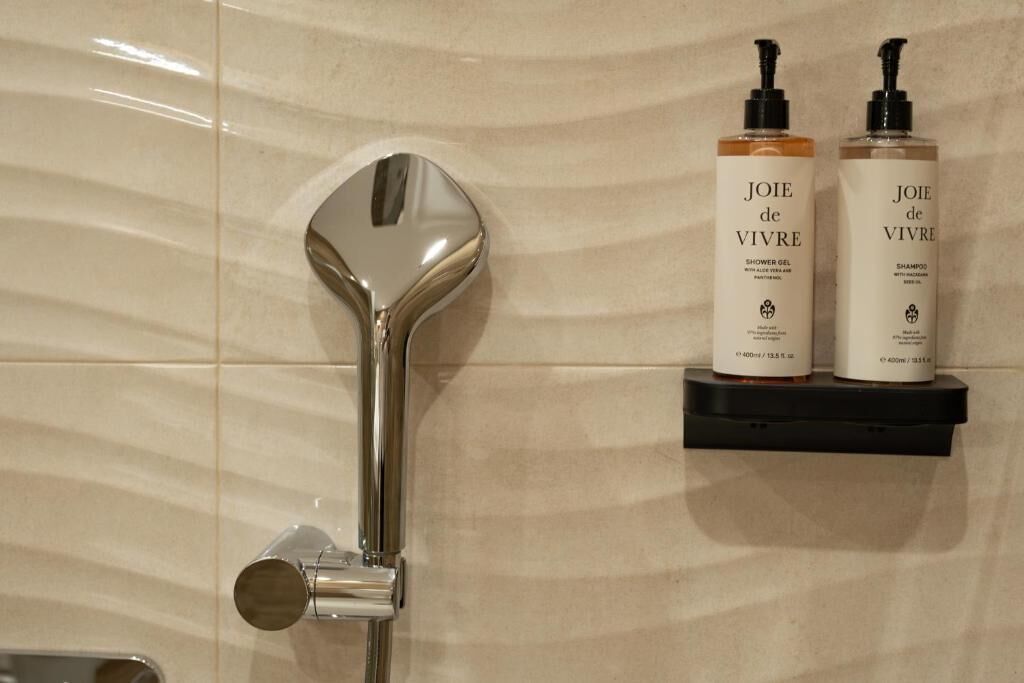A shower with a modern design, two bottles of Joie de Vivre shower gel and shampoo on a black shelf.