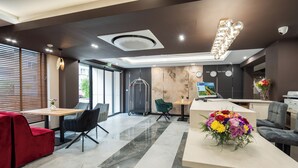 Una moderna hall d'albergo con una reception, una zona relax e una grande finestra con tende.