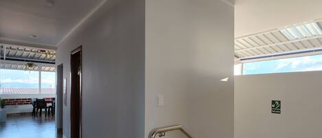 Interior limpo e moderno, com escada, vista para o exterior e sinalização de saída.