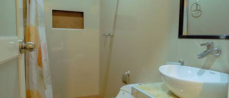 A bathroom with a toilet, sink, shower, and a trash bin.