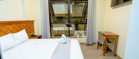 Habitación de hotel con una cama, cabecera de madera, una mesita y una ventana con cortinas.
