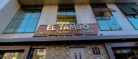 The exterior of the El Tambo Hotel in Tarapoto, Peru, featuring a modern facade with large windows and a prominent hotel sign.