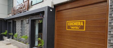 A hotel entrance with a sign reading "COCHERA HOTEL" and a sign above the door for "El Tambo".