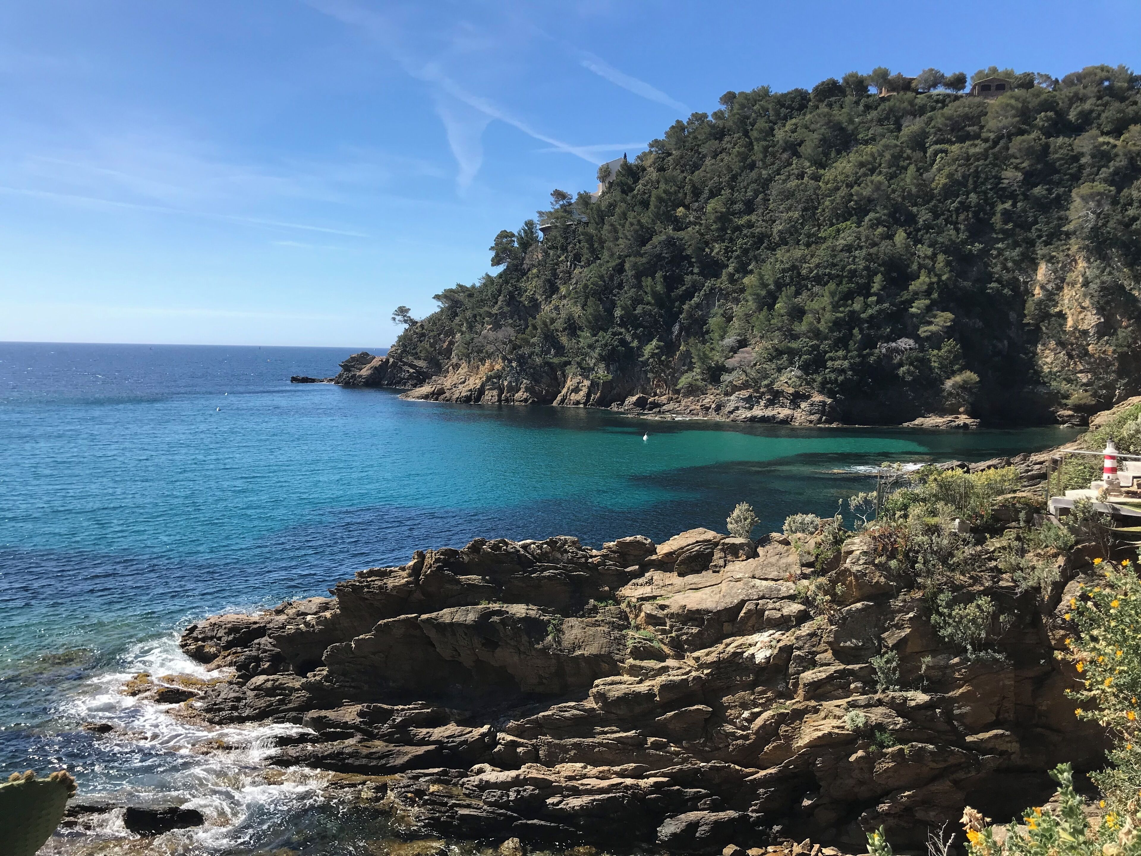 Un paysage côtier caractérisé par un terrain rocheux, des eaux d’un bleu limpide et une colline boisée.
