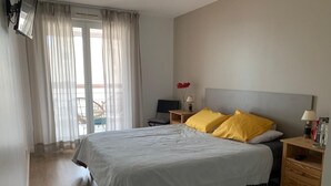 A bedroom with a large bed, two bedside tables, a chair, a desk, and a window with curtains. - Comfortable apartment 95 m2, 2 terraces, sea view, near beach, port, center (Cavalaire-sur-Mer)