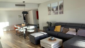 A modern living room with a grey sofa, a coffee table, and a dining area with chairs and a table. - Comfortable apartment 95 m2, 2 terraces, sea view, near beach, port, center (Cavalaire-sur-Mer)