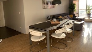A modern living room with a dining area, a sofa, and a large window with a view. - Comfortable apartment 95 m2, 2 terraces, sea view, near beach, port, center (Cavalaire-sur-Mer)