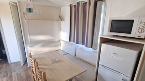A compact kitchenette with a microwave, a refrigerator, a wooden dining table, and a sofa.