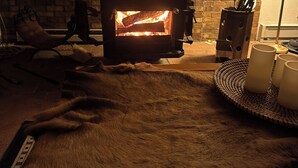 Una habitación acogedora con una estufa de leña, un tapete de piel y una mesa con velas.