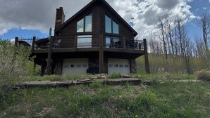 A two-story log cabin with a balcony, large windows, and a stone chimney.