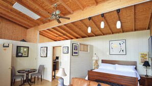 Una habitación con techo de madera, una cama, un sofá, una mesa con sillas y cuadros en las paredes.